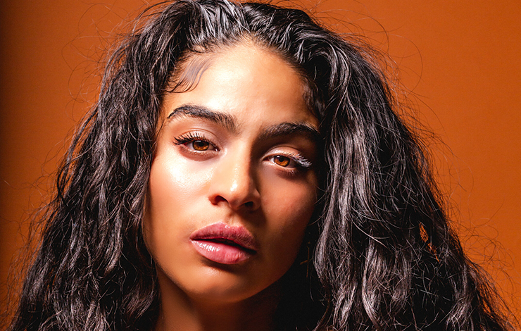 Jessie Reyez posing against an orange background