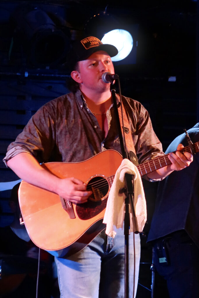 An artist, Riley Taylor, stands centre stage singing into the microphone on stage at Rivoli in Toronto.